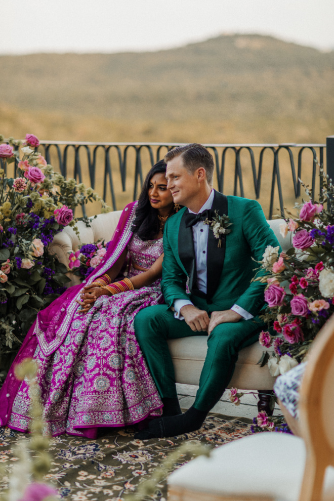The bride and groom sit on a couch at their outdoor Hindu wedding ceremony.