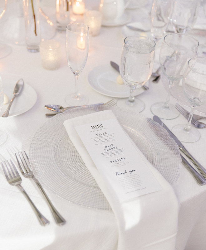 A menu atop a placesetting atop a table set with tablecloth and lit votives in a ballroom at Omni Houston Hotel. 