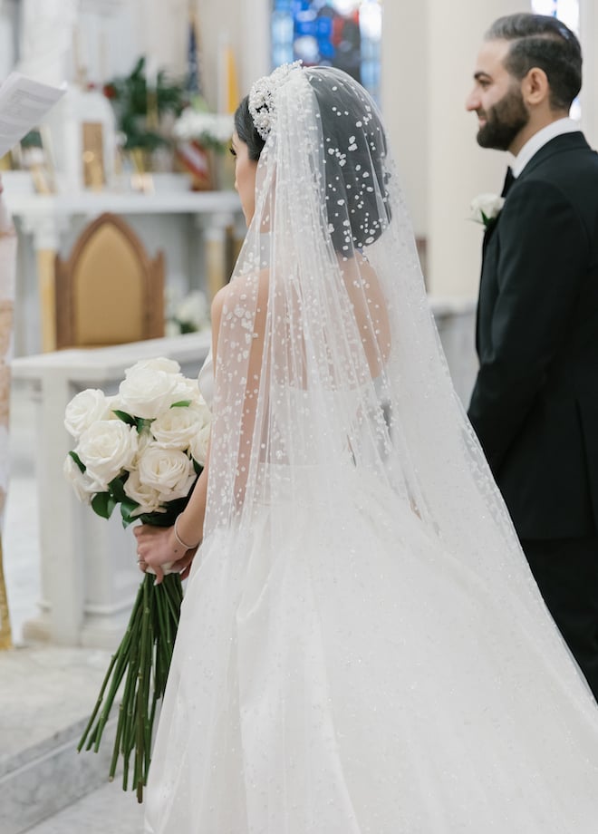 The bride holding a bouquet of white roses as she and the groom stand at the altar.