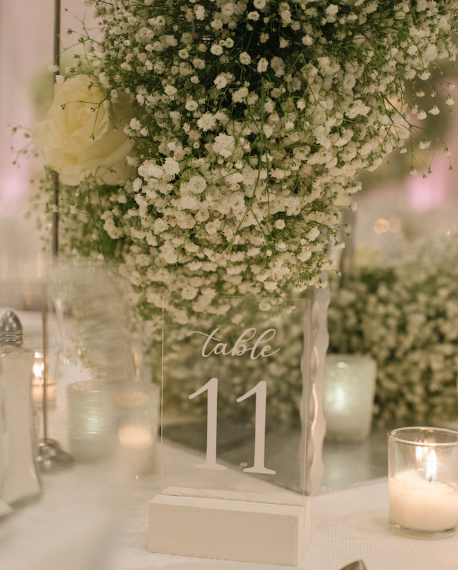 A lucite table number reading "table 11" aside baby's breath and lit votives 