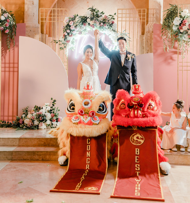 The bride and groom holding their hands in the air in front of the lion dancers.