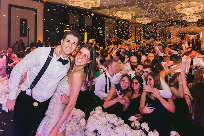 Caitlin and Max smiling on stage at their opulent ballroom wedding.