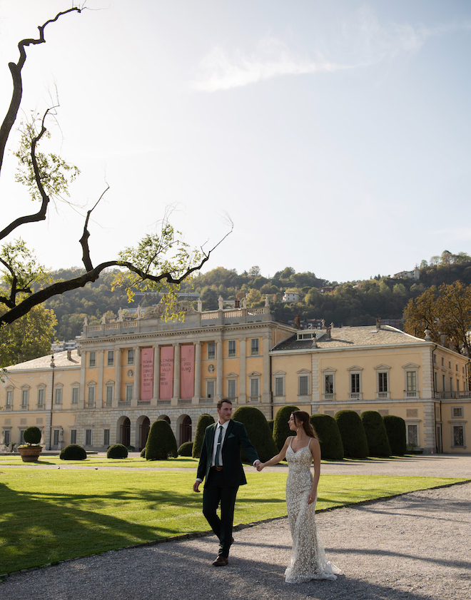 The bride and groom holding hands as they walk in front of Villa Olmo.
