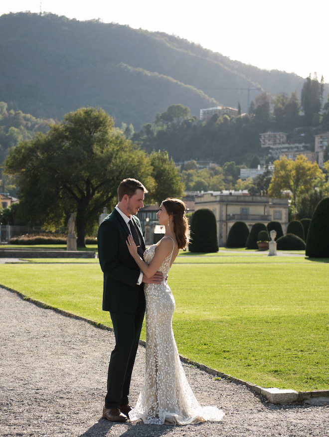 The bride and groom facing each other with greenery and mountains behind them.