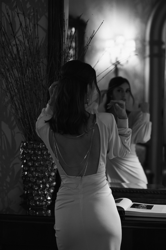 The bride putting on her earrings facing a mirror.