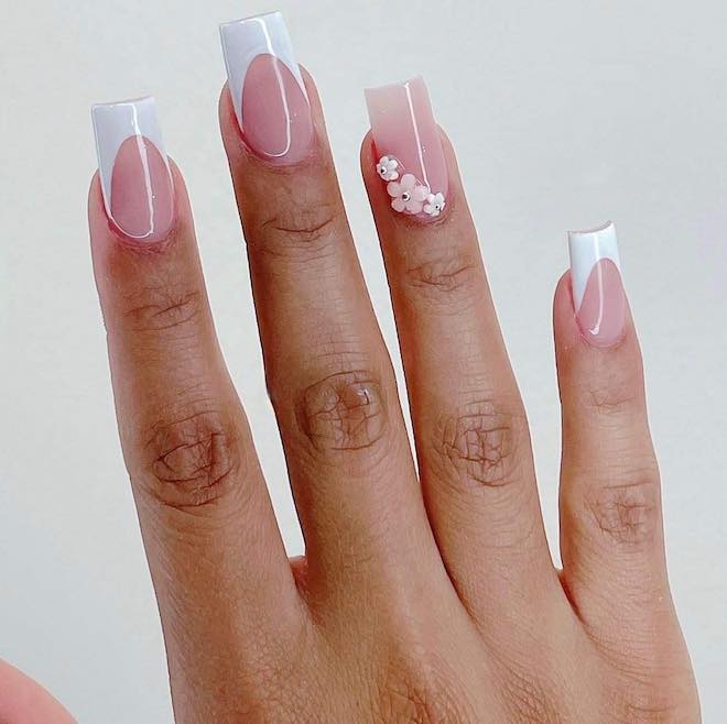 French manicure with a floral charm on the ring finger.