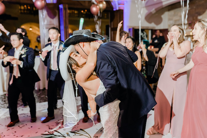 The bride and groom kissing on the dance floor with cowboy hats on.