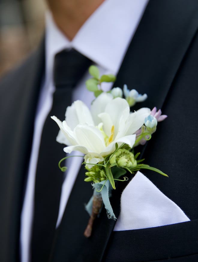 The groom wears a white flower as his boutonniere on his tuxedo. 