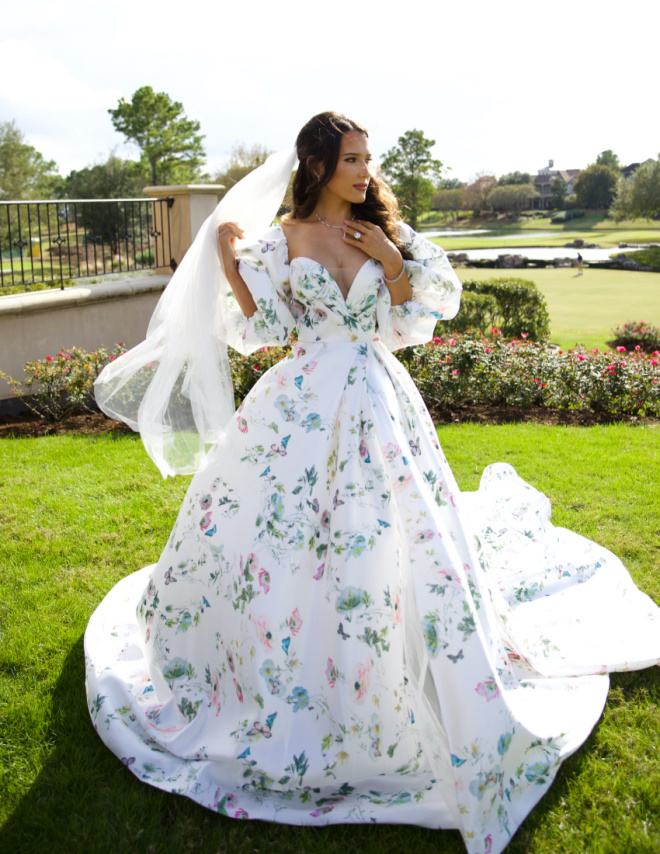 The bride models a non-traditional white and pastel floral detailed wedding gown from Belle Ame Bridal.