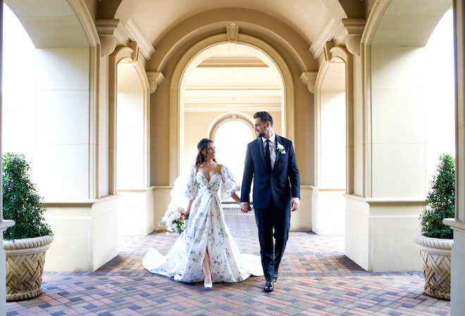 The bride and groom hold hands and walk outside of the wedding venue at The Royal Oaks Country Club. 