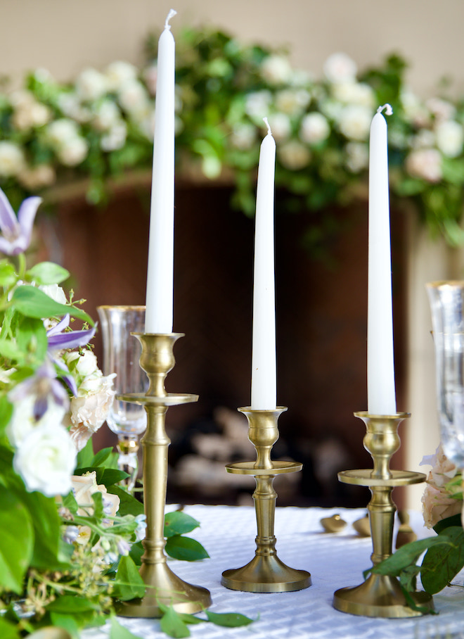 White candlesticks are placed on gold candle holders to set the table space for the whimsical and romantic wedding editorial. 
