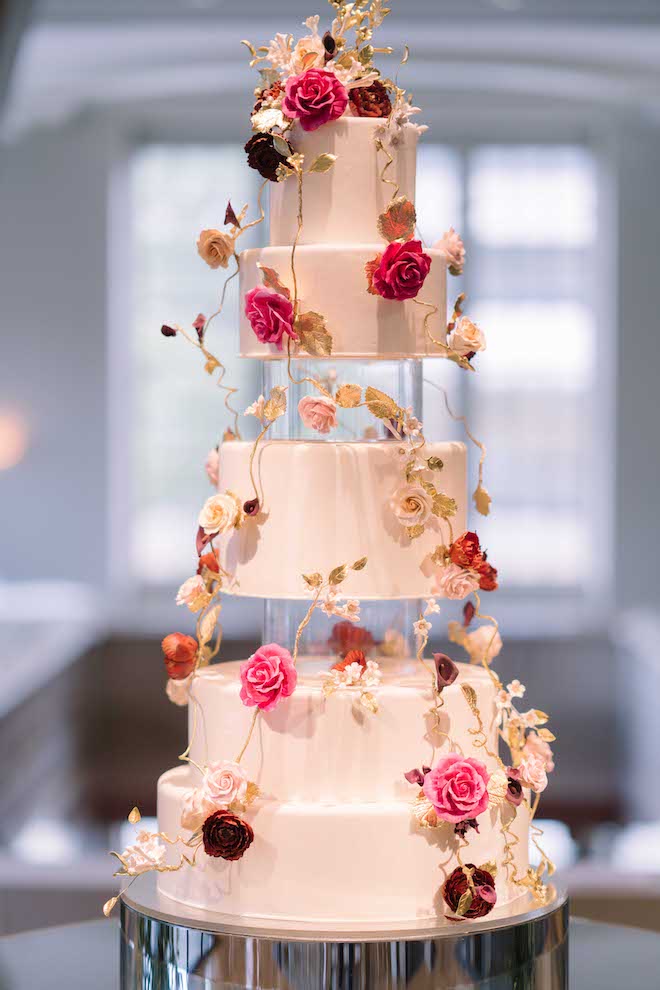 A five-tier wedding cake with two clear tiers covered in roses and vines.