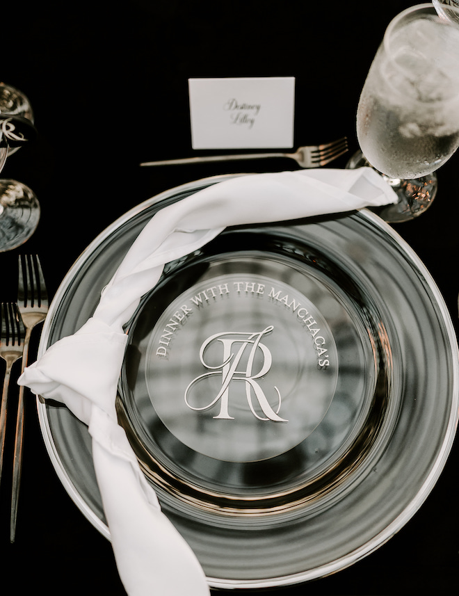 A clear plate with a logo with the couple's monogram and "Dinner with the Manchaca's".