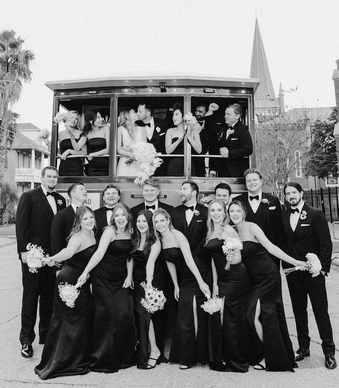 The bride and groom kissing on the Galveston Trolley as the bride party smiles around them.