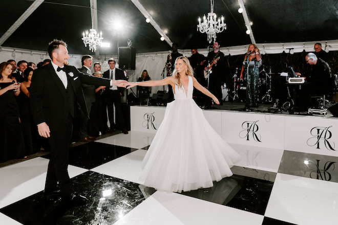 The bride and groom holding hands while dancing on a black and white dance floor. 