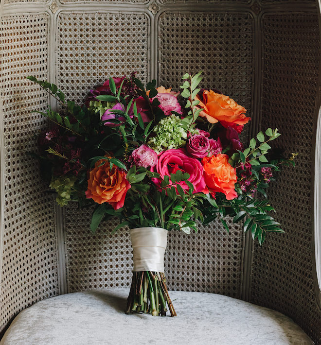 A bouquet sitting in a chair with greenery, pink and orange florals. 
