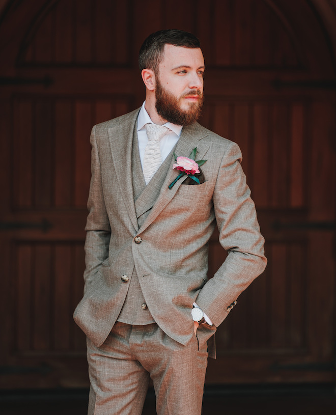 The groom wearing a gray suit with a pink flower pinned to his jacket. 