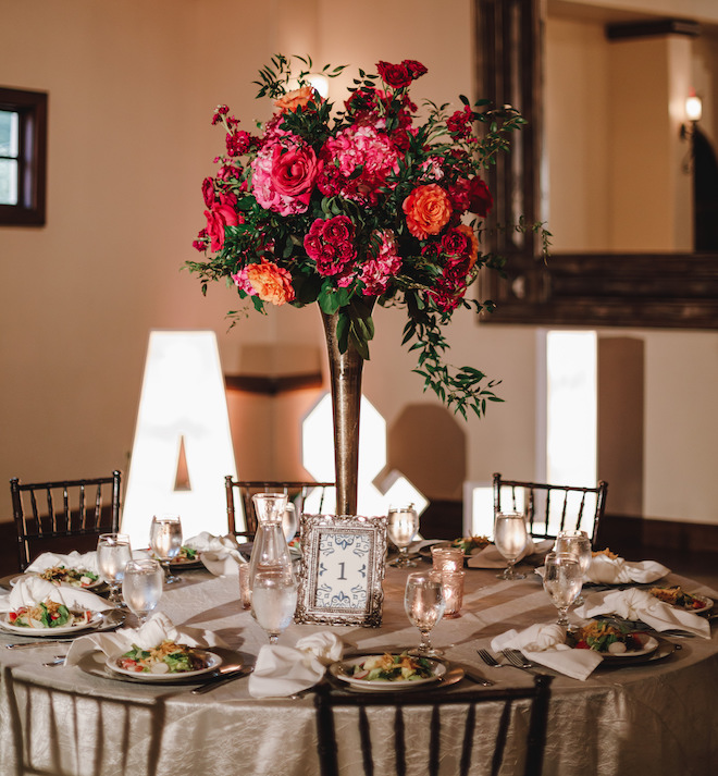 A round reception table with a centerpiece of vibrant pink and orange floral arrangements. 