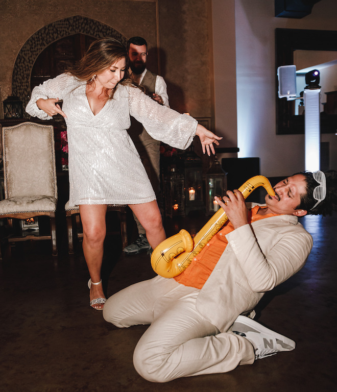 The bride dancing with a guest who is playing a blow-up saxophone. 