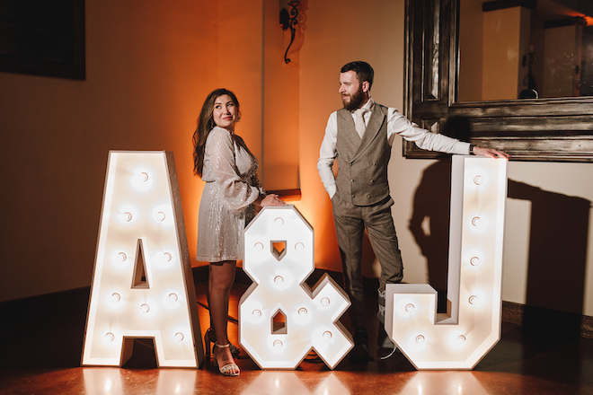 The bride and groom posing with lit-up marquee "A & J" letters.