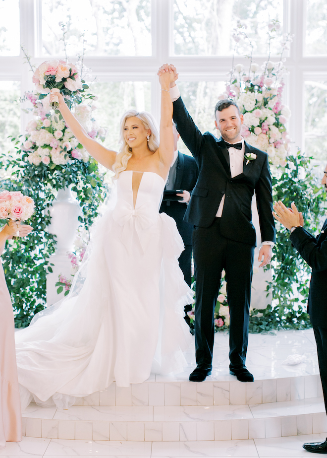 The bride and groom lifting their hands up in the air at the altar after their wedding ceremony. 