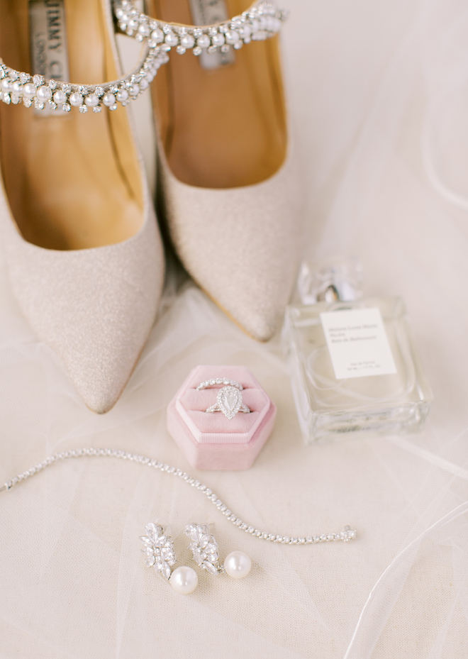 A pair of nude Jimmy Choo shoes with crystals, a pink ring box with a engagement and wedding band, a diamond necklace and earrings.