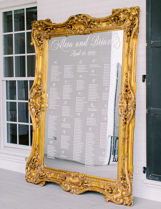 A gold framed mirror with Alexa and Brian's wedding seating chart etched on the glass. 