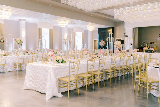 Long white tables with gold chairs and light and bright pink and ivory florals as centerpieces.
