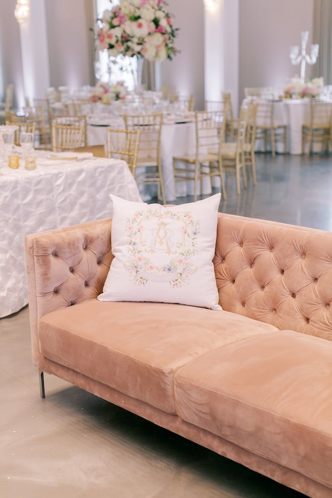A pink couch with a white pillow with pastel floral print and the couple's initials. 