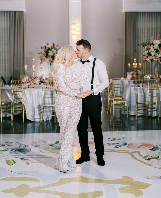 The bride and groom kissing on the custom dance floor. The bride is wearing an all-lace jumpsuit. 