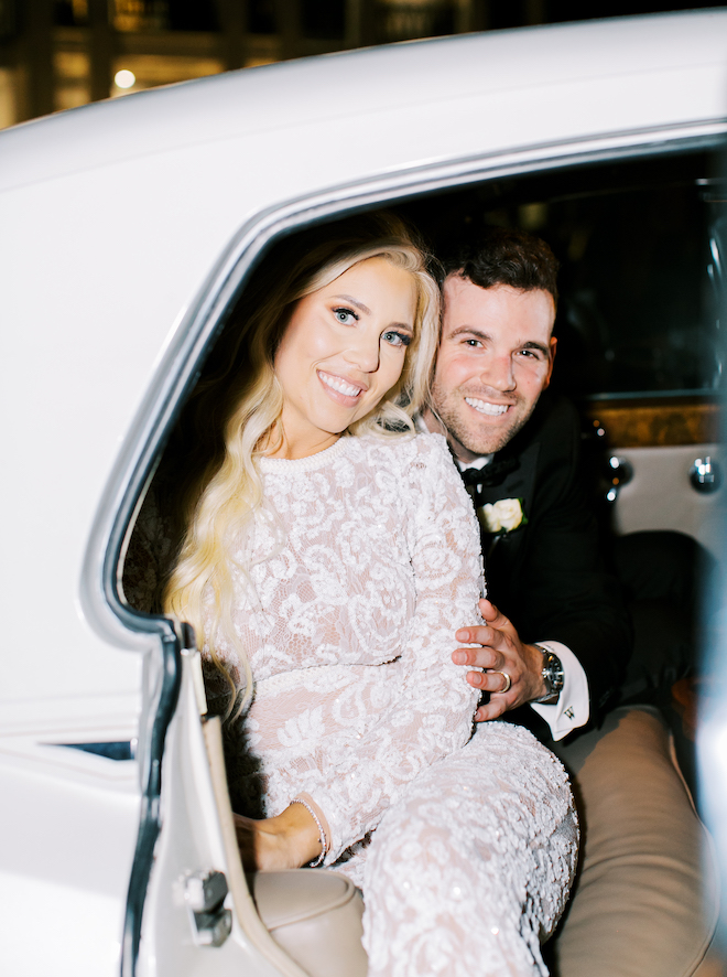 The bride and groom smiling in a white vintage car. 