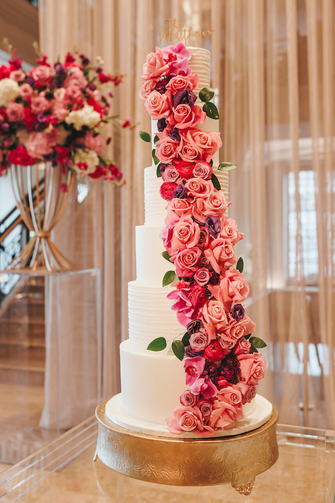 A six tier white wedding cake with pink and purple roses. 