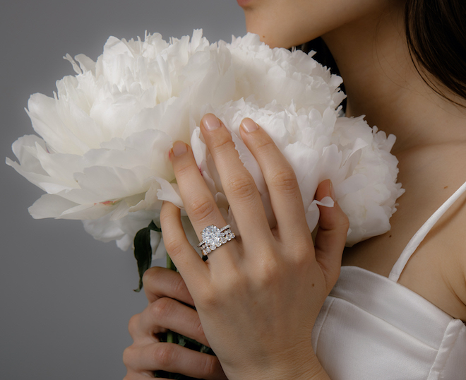 A woman with a large engagement ring on holding a white flower.