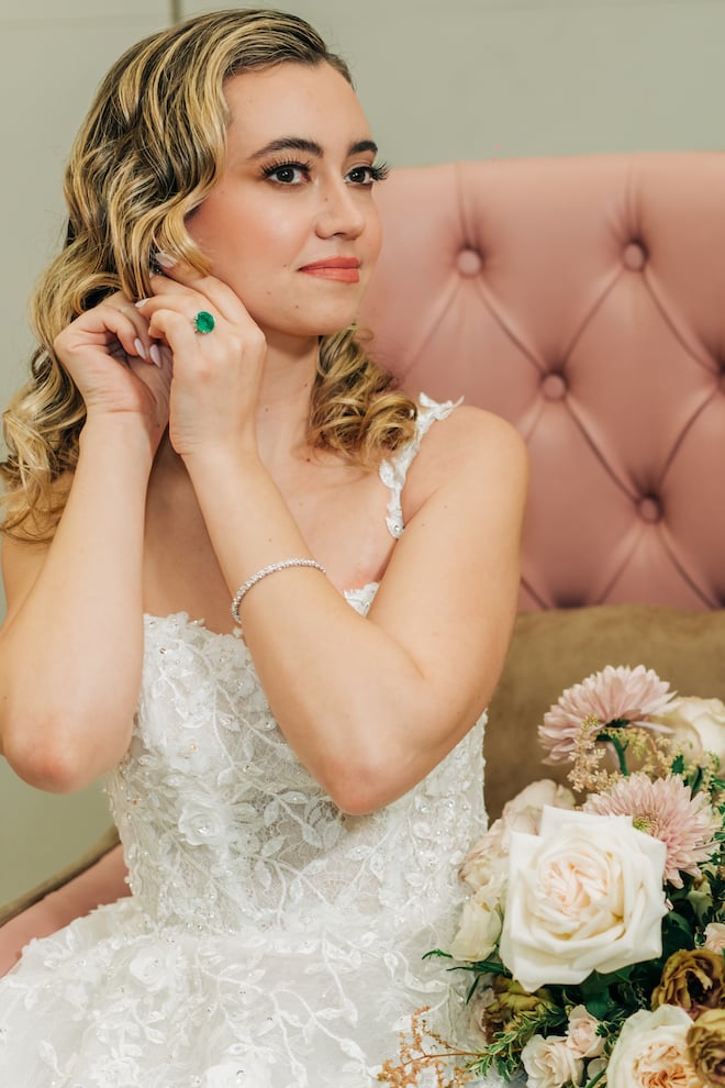 The bride adjusting her earring as she wears her emerald green wedding ring. 