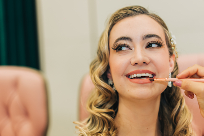The bride smiling as she gets her lipstick applied.