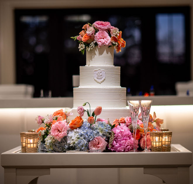 A four tier white wedding cake garnished with colorful flowers for an elegant spring wedding.