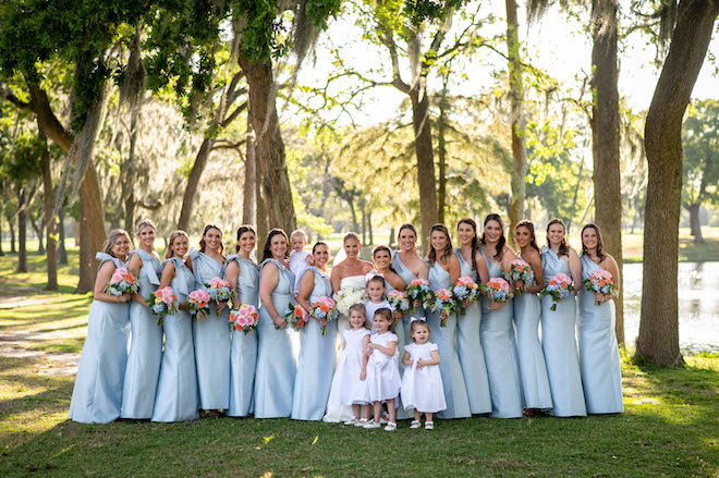 The bride smiling with her bridal party wearing light blue gowns and the flower girls in white dresses.