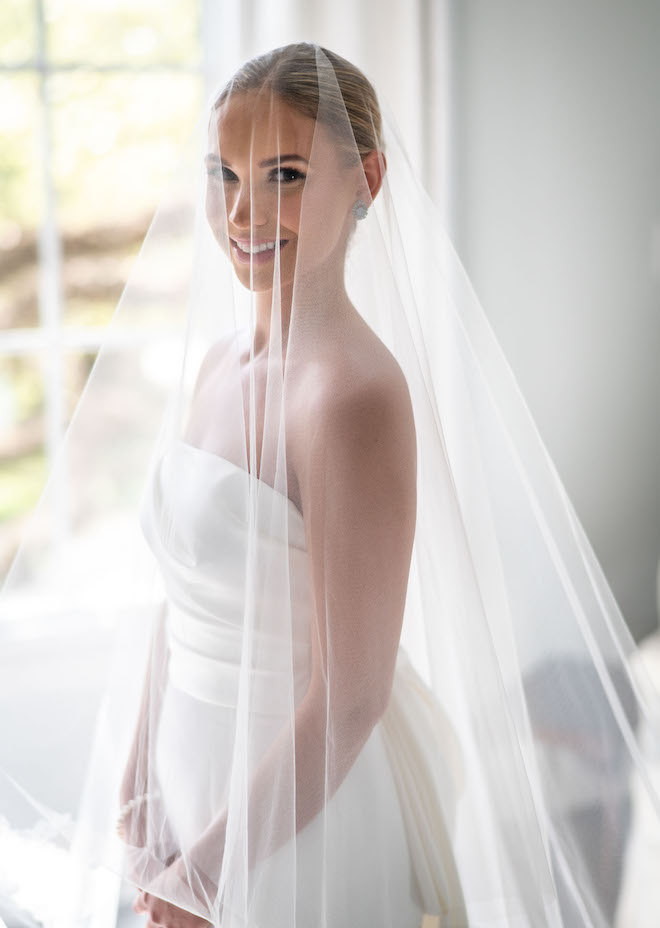 The bride smiling in her strapless white wedding gown and veil.