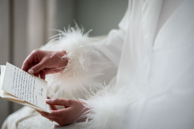 The bride wearing a feathered pajama top and holding a letter from the groom.