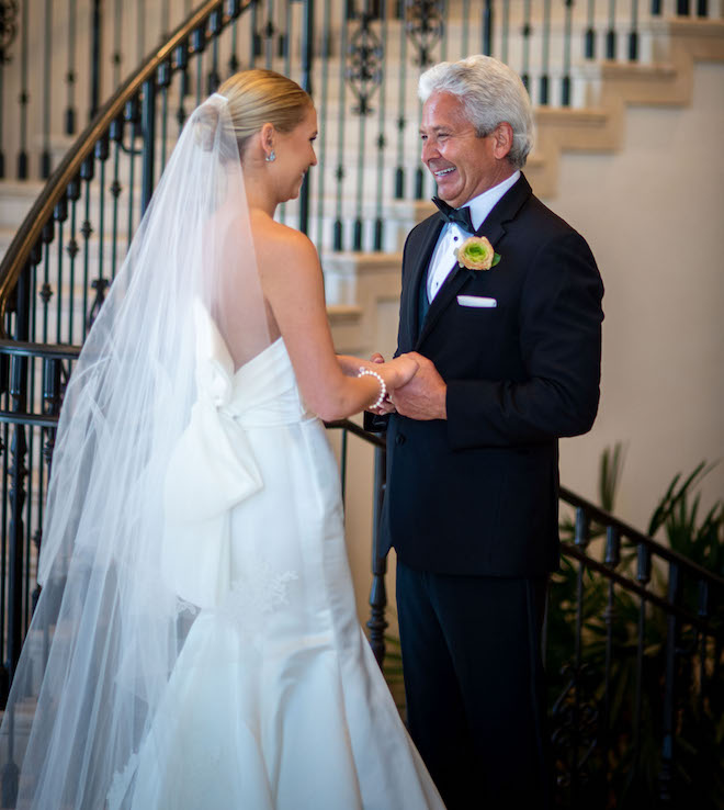 The bride and her father smiling as they hold hands.