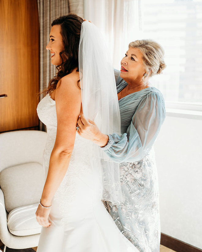 The mother of the bride helping the bride put on her veil.