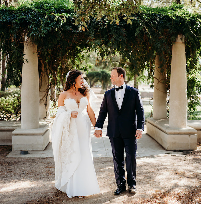 The bride and groom smiling at each other and holding hands as they walk.