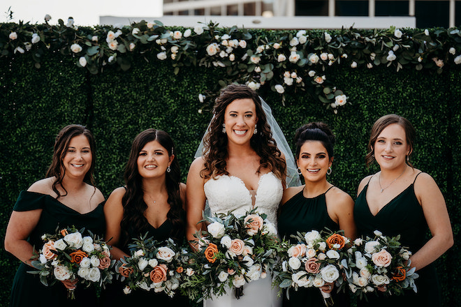The bride smiling with her four bridesmaids holding bouquets and wearing emerald green dresses.