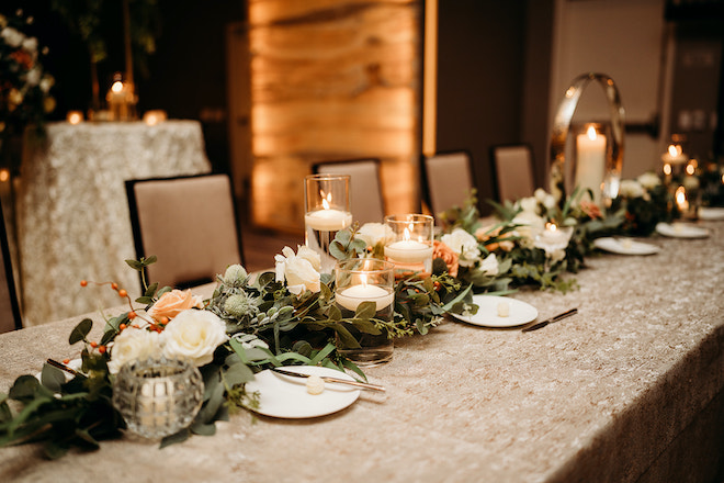 Candles and lush greenery with florals decorating the long reception table.