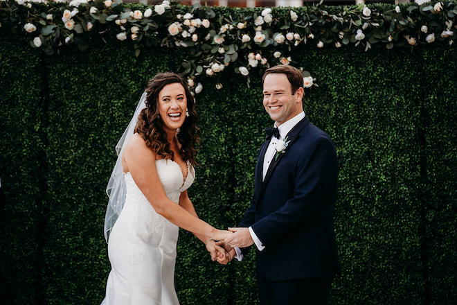 The bride and groom holding hands and laughing during their rooftop wedding ceremony.