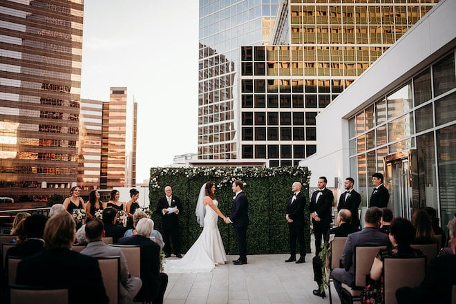 The bride and groom holding hands during their rooftop wedding ceremony with the medical buildings in the background.