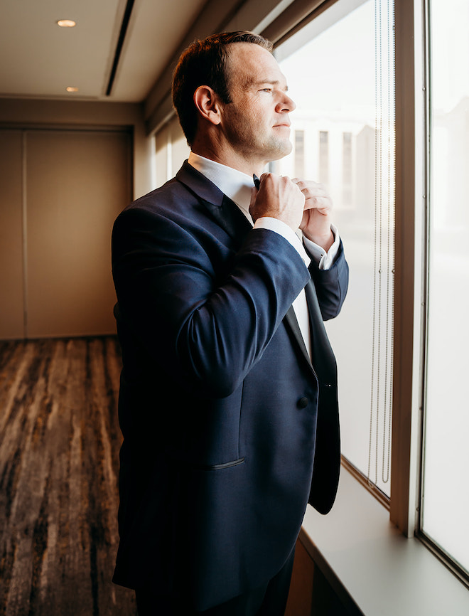 The groom adjusting his bow tie and looking out the window before the rooftop wedding ceremony at the Westin Houston Medical Center.