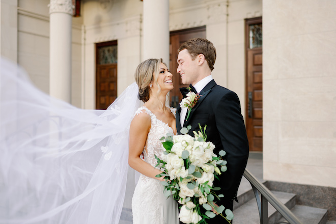 The bride and groom smiling at each other as the bride's veil flows in the wind.