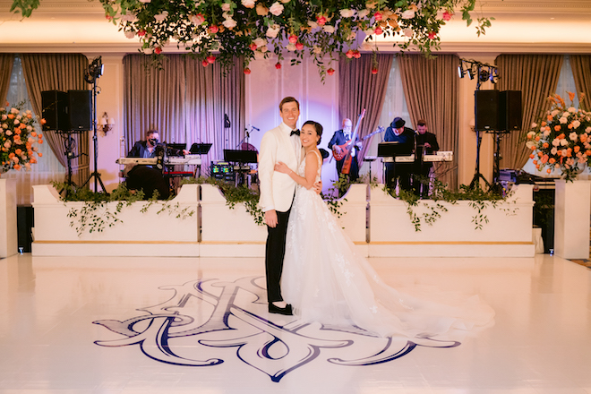 The bride and groom smiling on the white dance floor with their blue monogram. 