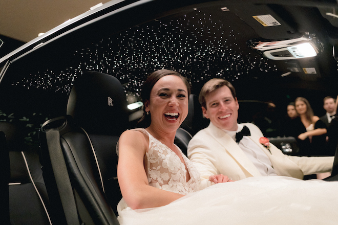 The bride and groom smiling in their getaway car. 
